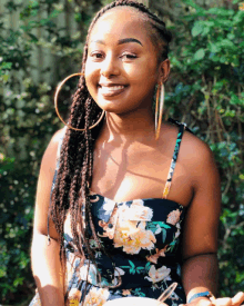 a woman in a floral dress and hoop earrings smiles for the camera