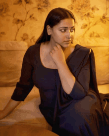 a woman in a black dress sits on a couch with her hand on her chin