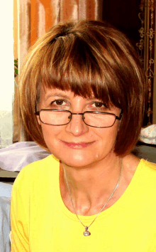 a woman wearing glasses and a yellow shirt looks at the camera