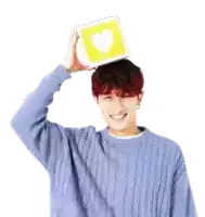 a man wearing a blue sweater is holding a yellow block with a heart on it on his head .