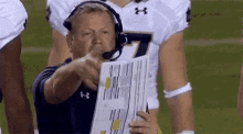 a man wearing a headset is pointing at something while holding a piece of paper on a football field .