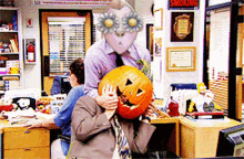 a man is holding a pumpkin in front of his face in an office with a smoking sign on the wall