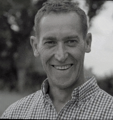 a man wearing a plaid shirt smiles for the camera