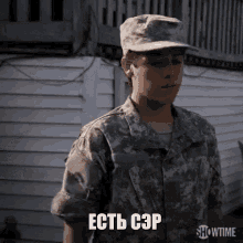 a young man in a military uniform is standing in front of a white house and talking in a foreign language .