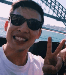 a man wearing sunglasses giving a peace sign in front of a bridge