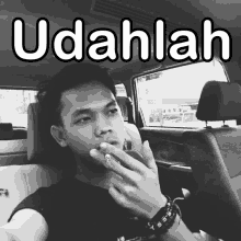 a man smoking a cigarette in a car with the words udahlah on the bottom