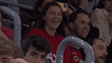 a group of people sitting in a stadium with one wearing a red shirt that says ' athletic ' on it