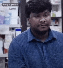 a man in a blue shirt is standing in front of a shelf in a pharmacy and making a funny face .