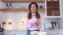 a woman wearing a pink and white striped shirt and a black hat is standing in a kitchen with a bosch toaster