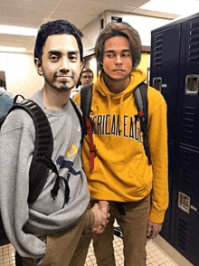 a man wearing a yellow american eagle sweatshirt shakes hands with a man wearing a grey sweatshirt