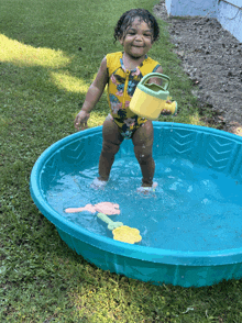 a little girl in a yellow swimsuit is standing in a pool of water holding a watering can