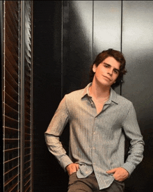 a young man in a striped shirt leans against a wall