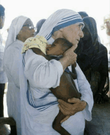 a woman holding a baby in her arms with a group of women behind her