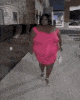 a woman is walking down a sidewalk wearing a pink dress .