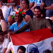 a group of people are sitting in a stadium watching a game and one of them is holding a flag .