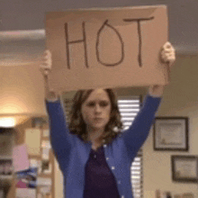 a woman in a blue sweater is holding a sign that says hot