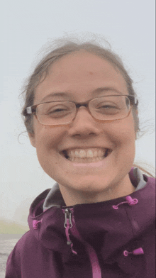 a woman wearing glasses and a purple jacket smiles at the camera