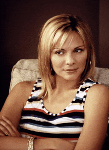 a woman in a striped tank top is sitting in a chair with her arms crossed