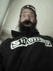 a man with a beard wears a black shirt that says sham