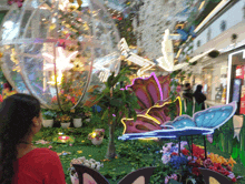 a woman in a red shirt is looking at a display of flowers and butterflies