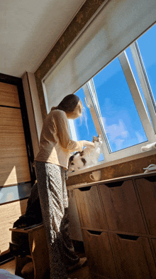 a woman petting a cat while looking out a window