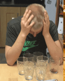 a man wearing a nike shirt is sitting at a table with empty glasses