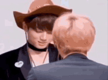 a man wearing a cowboy hat and a choker is kissing another man .