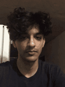 a young man with curly hair and a black shirt looks at the camera