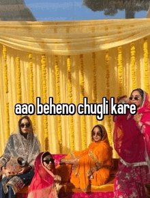 a group of women sitting in front of a yellow curtain with the words aao beheno chugli kare written on it