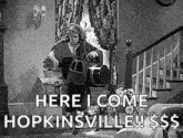 a black and white photo of a man standing in a living room with a bucket and a dog .