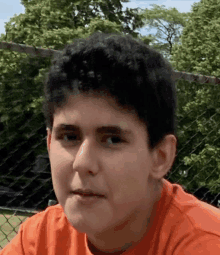 a young man wearing an orange shirt is looking at the camera