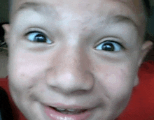 a close up of a child 's face with a red shirt on making a funny face