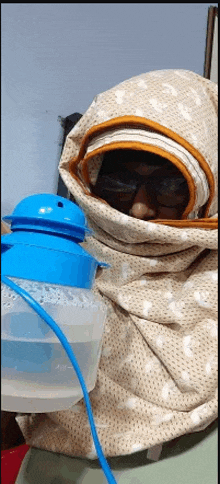 a person wrapped in a blanket is holding a blue bottle of water .