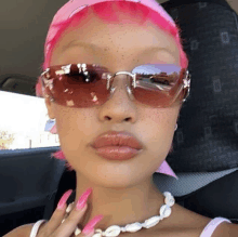 a woman with pink hair is wearing sunglasses and a pink bandana .