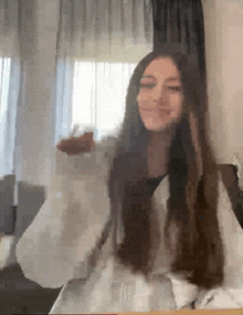 a woman with long hair is sitting at a table with her arms outstretched in front of a window .