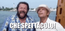 two men are standing next to each other on a boat with the words che spettacolo written on the bottom .