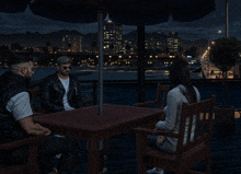 a group of people sit at a table under an umbrella