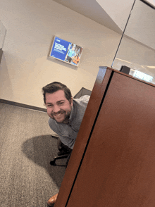 a man is peeking out from behind a desk in front of a sign that says ' aoc ' on it