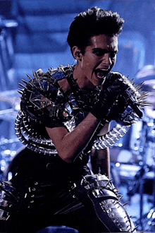 a man singing into a microphone with spikes on his arms and chest