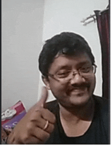 a man wearing glasses is giving a thumbs up sign .