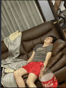 a man is sleeping on a couch with a bottle of coca cola next to him