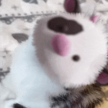 a stuffed animal with pink ears and a black spot on its face is laying on a bed .