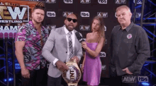 a man in a suit is holding a wrestling championship belt while standing next to two other men and a woman .