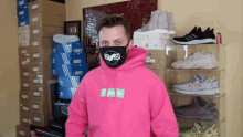 a man wearing a mask and a pink hoodie stands in front of a pile of shoes