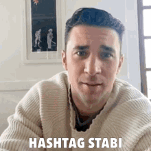 a man in a sweater says " hashtag stabi " in front of a picture