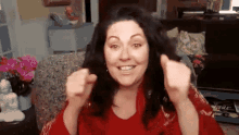 a woman in a red shirt is giving a thumbs up while sitting in a chair in a living room .