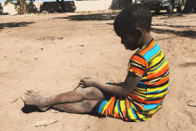 a boy in a colorful striped shirt sits on the sand