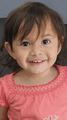 a little girl wearing a pink shirt with a heart on it is smiling