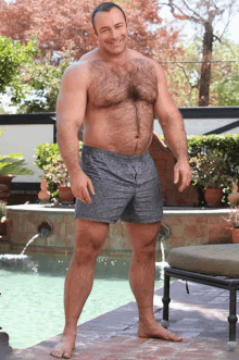 a shirtless man in gray shorts is standing next to a pool