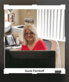 a woman in a red shirt is sitting at a desk in front of a computer monitor .